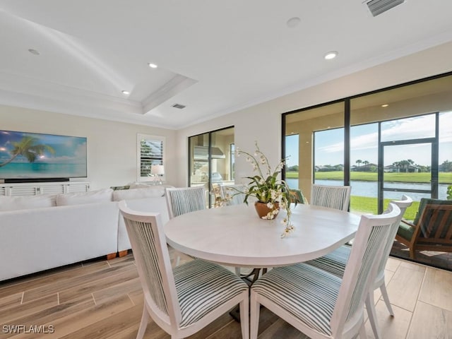 dining room with ornamental molding, a water view, and a tray ceiling