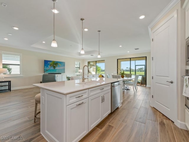 kitchen featuring decorative light fixtures, an island with sink, stainless steel dishwasher, and white cabinetry