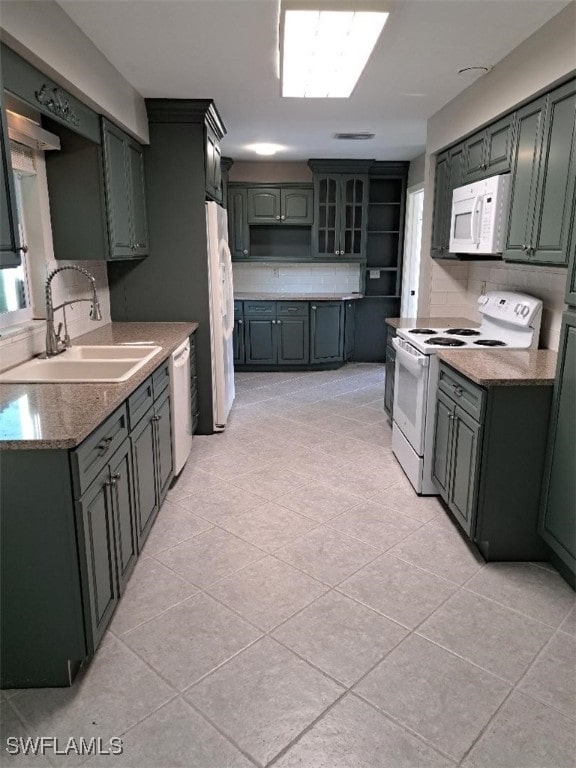 kitchen featuring a skylight, sink, backsplash, white appliances, and light tile patterned floors