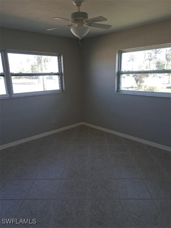 empty room with a wealth of natural light, ceiling fan, and dark tile patterned flooring