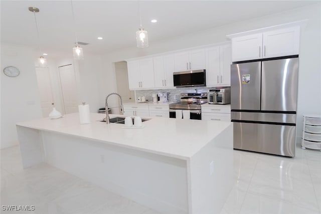 kitchen featuring stainless steel appliances, a kitchen island with sink, sink, pendant lighting, and white cabinetry