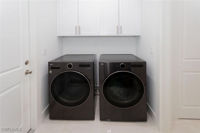 clothes washing area with washer and dryer, light tile patterned flooring, and cabinets