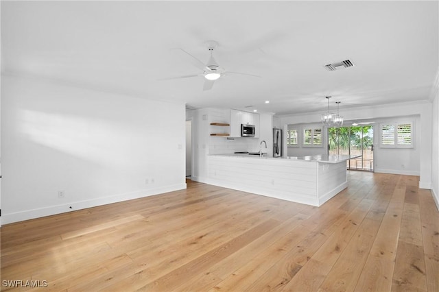 unfurnished living room with visible vents, light wood-style flooring, a sink, baseboards, and ceiling fan with notable chandelier