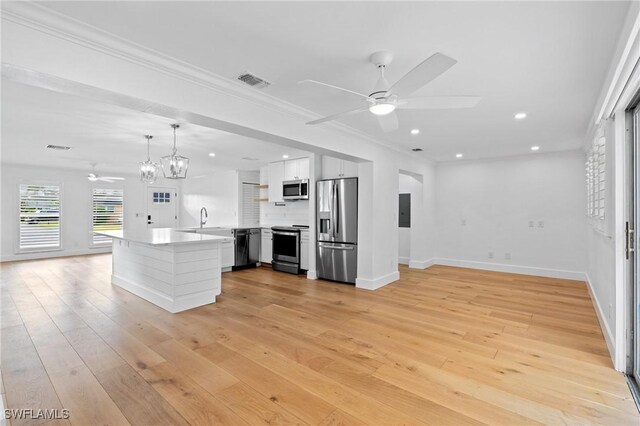 kitchen featuring pendant lighting, backsplash, white cabinets, ornamental molding, and appliances with stainless steel finishes