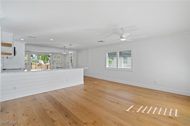 unfurnished living room with baseboards, ceiling fan with notable chandelier, visible vents, and light wood-style floors