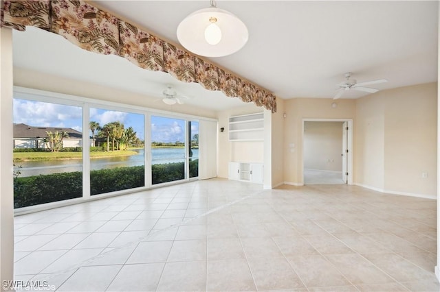 spare room featuring built in features, light tile patterned floors, a water view, and ceiling fan