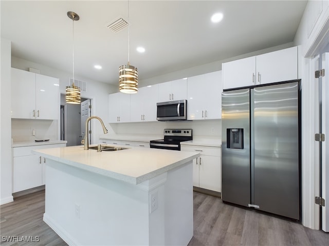 kitchen featuring appliances with stainless steel finishes, a kitchen island with sink, sink, pendant lighting, and white cabinetry