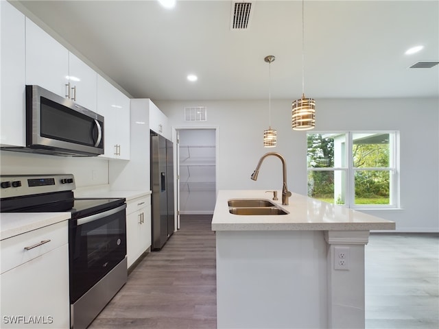 kitchen with white cabinets, a center island with sink, sink, hanging light fixtures, and stainless steel appliances