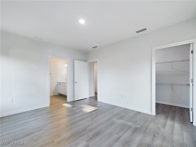 unfurnished bedroom featuring light wood-type flooring, a walk in closet, a closet, and connected bathroom