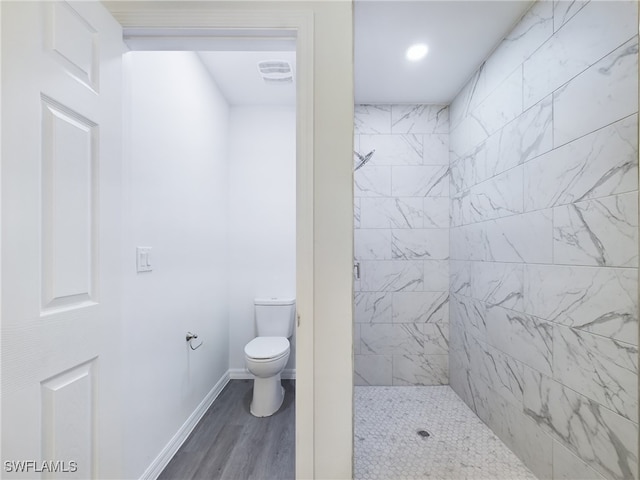 bathroom with hardwood / wood-style flooring, toilet, and tiled shower