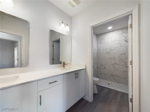 bathroom with hardwood / wood-style floors, vanity, toilet, and tiled shower