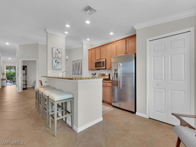 kitchen featuring light tile patterned flooring, appliances with stainless steel finishes, a center island, light stone counters, and crown molding