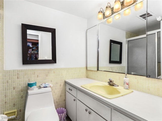 bathroom featuring vanity, toilet, a shower with door, and tile walls