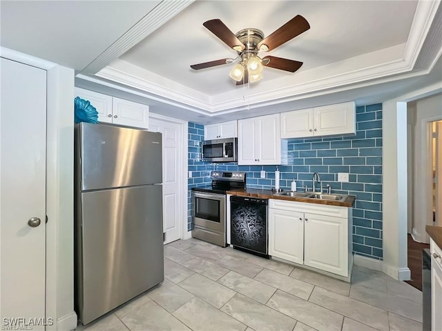 kitchen featuring white cabinets, sink, ceiling fan, a tray ceiling, and stainless steel appliances