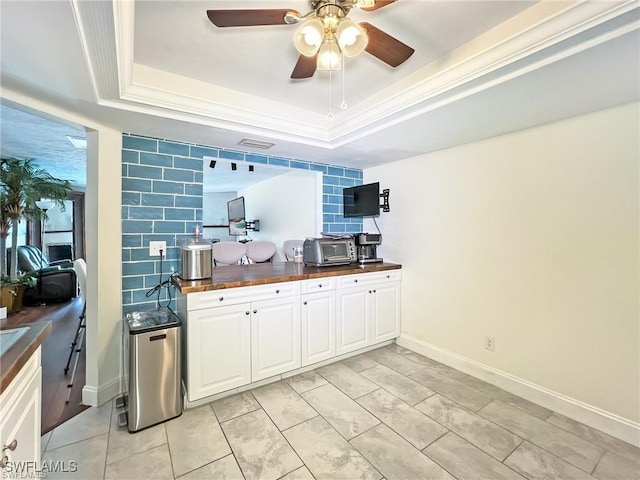 kitchen featuring a raised ceiling, ceiling fan, crown molding, butcher block countertops, and white cabinetry