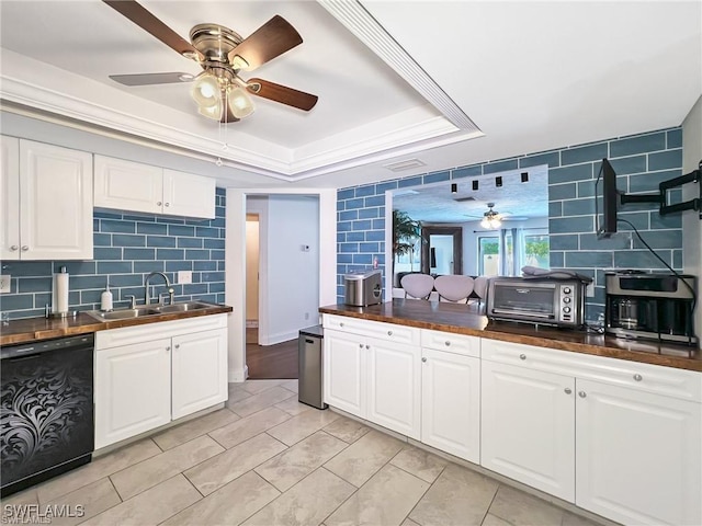 kitchen featuring white cabinets, tasteful backsplash, a tray ceiling, sink, and dishwasher