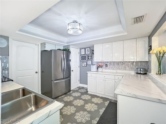 kitchen featuring white cabinets, a tray ceiling, stainless steel refrigerator, and sink