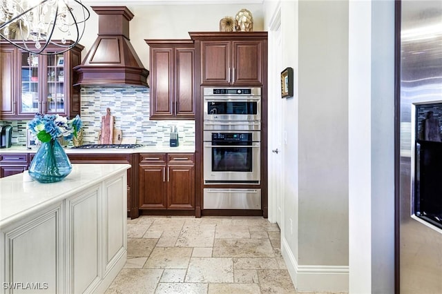 kitchen with stainless steel appliances, custom exhaust hood, hanging light fixtures, and decorative backsplash