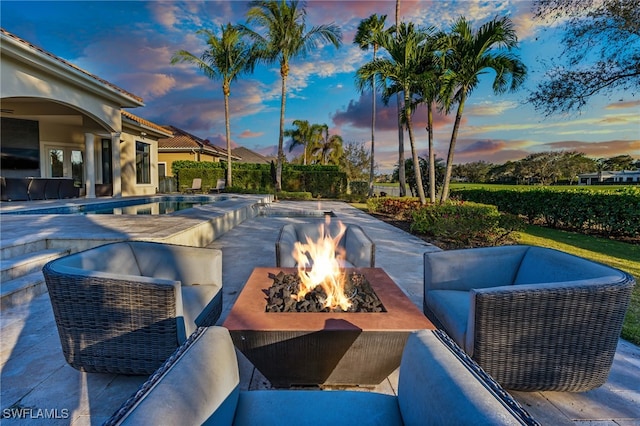 pool at dusk with an outdoor fire pit and a patio