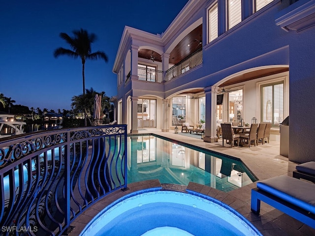 pool at night with a pool with connected hot tub, a patio, and a ceiling fan