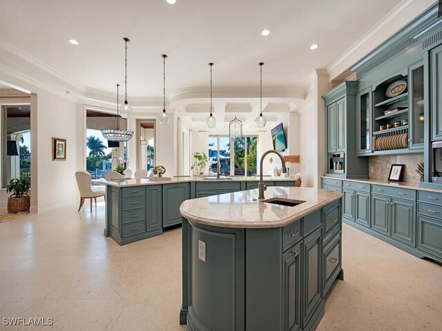 kitchen featuring a kitchen island with sink, glass insert cabinets, decorative backsplash, hanging light fixtures, and a sink