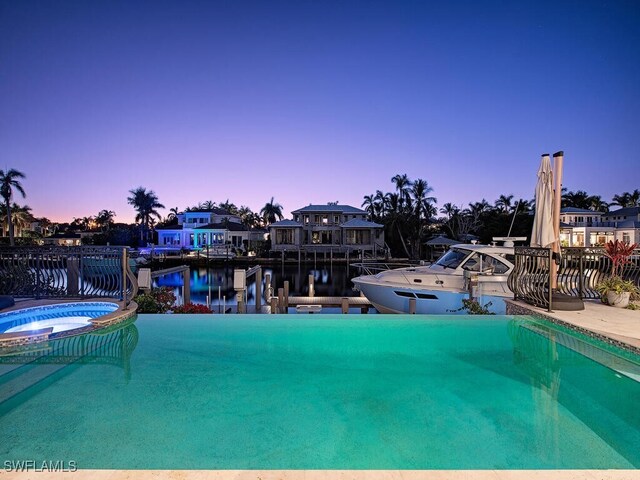 view of pool featuring a water view, fence, a dock, and a pool with connected hot tub