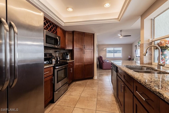 kitchen with light stone countertops, stainless steel appliances, tasteful backsplash, sink, and a raised ceiling