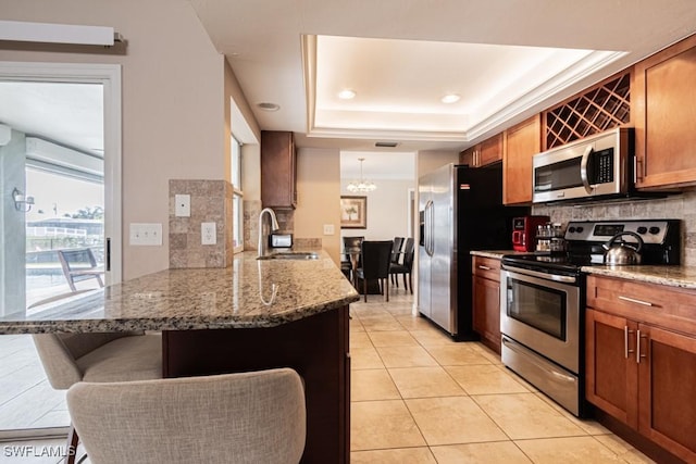 kitchen featuring kitchen peninsula, appliances with stainless steel finishes, sink, a tray ceiling, and a breakfast bar area