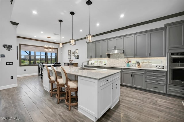 kitchen with gray cabinetry, pendant lighting, a center island with sink, and double oven