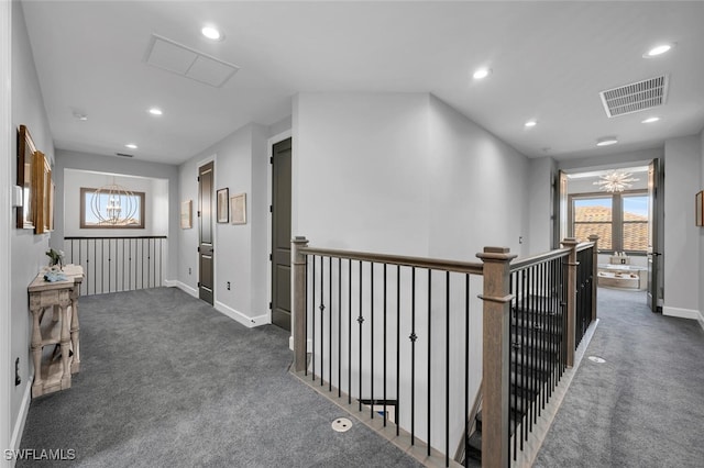 corridor featuring an inviting chandelier and dark colored carpet