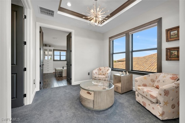 living area with a raised ceiling, ornamental molding, a notable chandelier, and dark colored carpet