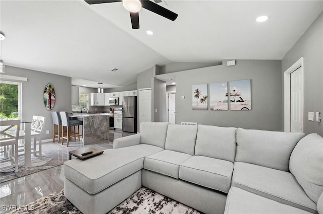 living room with ceiling fan, sink, lofted ceiling, and light wood-type flooring