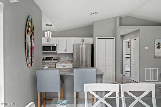 kitchen with white cabinetry, decorative light fixtures, vaulted ceiling, a kitchen bar, and appliances with stainless steel finishes