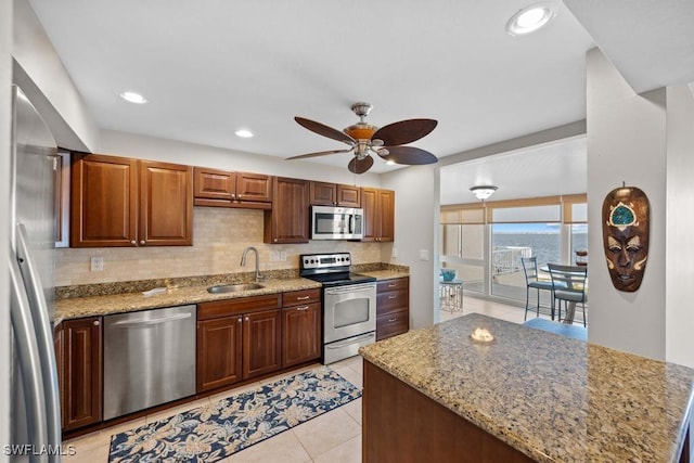 kitchen featuring sink, ceiling fan, decorative backsplash, light stone countertops, and stainless steel appliances