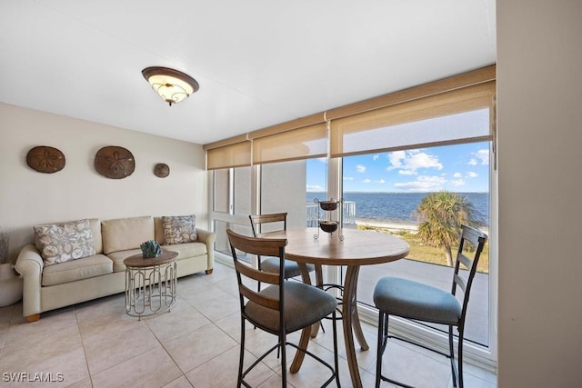 tiled dining room featuring a view of the beach, a water view, and a wall of windows