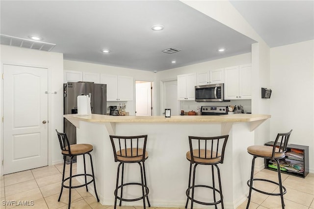 kitchen featuring stainless steel appliances, a breakfast bar area, white cabinetry, and light tile patterned floors