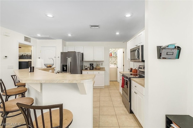 kitchen with stainless steel appliances, washer / dryer, a breakfast bar area, white cabinets, and light tile patterned flooring