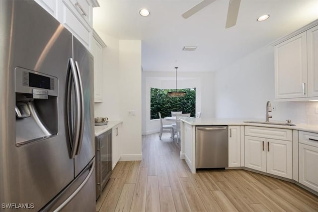 kitchen featuring appliances with stainless steel finishes, decorative light fixtures, sink, white cabinets, and light wood-type flooring