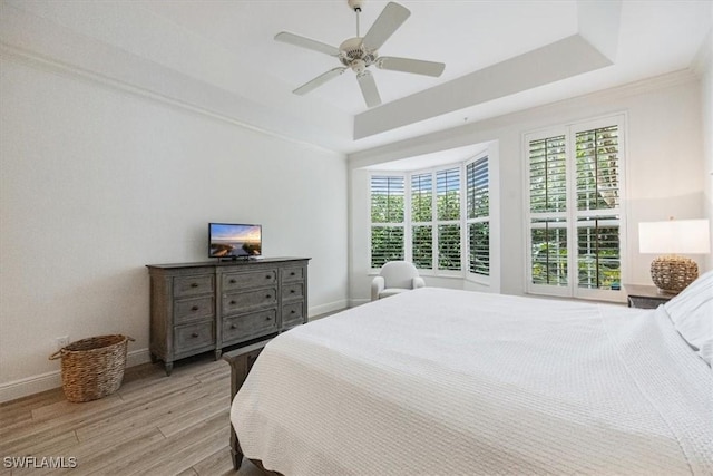 bedroom with a raised ceiling, light wood-type flooring, and ceiling fan