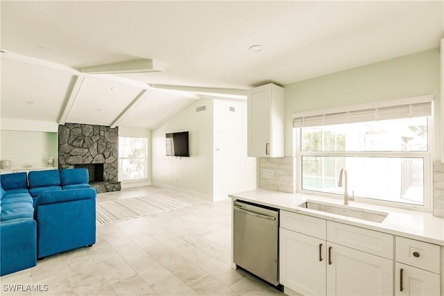 kitchen featuring white cabinetry, sink, stainless steel dishwasher, lofted ceiling with beams, and a fireplace