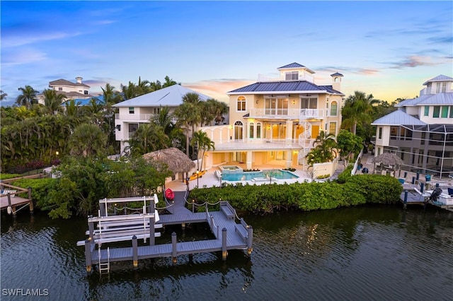 back house at dusk with a balcony, a water view, and a patio