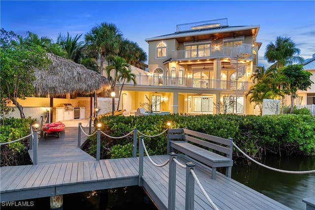 back house at dusk with an outdoor kitchen, a balcony, and a water view