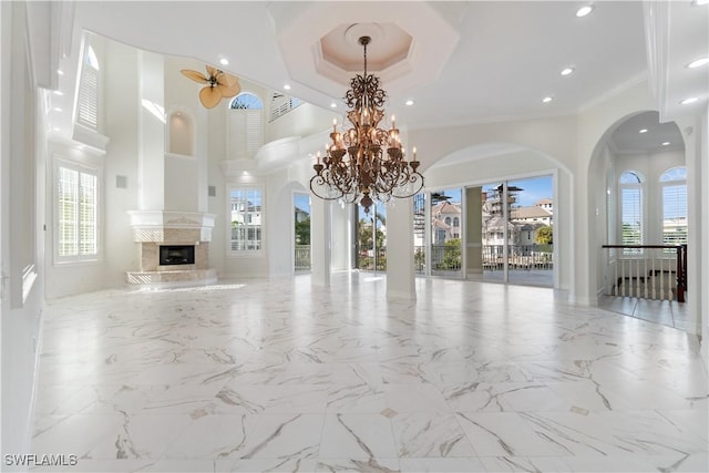 unfurnished living room featuring a raised ceiling, a premium fireplace, crown molding, and a high ceiling