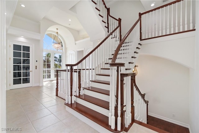 stairs with french doors, crown molding, a notable chandelier, tile patterned flooring, and a high ceiling