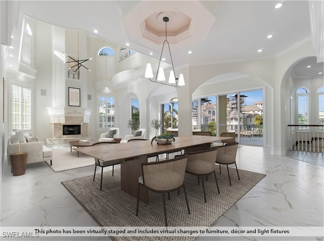 dining area featuring a high end fireplace, a raised ceiling, crown molding, a towering ceiling, and a chandelier