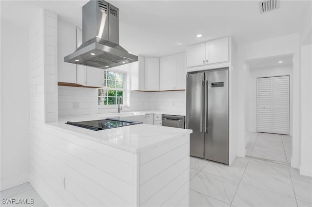 kitchen with tasteful backsplash, kitchen peninsula, white cabinets, exhaust hood, and appliances with stainless steel finishes