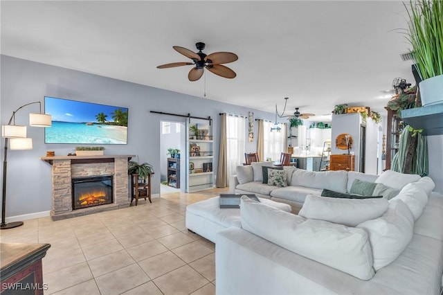 living room featuring ceiling fan, a barn door, a stone fireplace, and light tile patterned floors