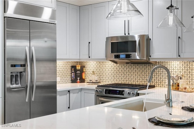 kitchen featuring sink, light stone counters, hanging light fixtures, appliances with stainless steel finishes, and decorative backsplash