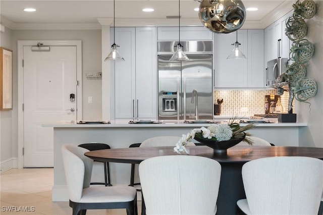 kitchen featuring crown molding, built in refrigerator, backsplash, light tile patterned flooring, and decorative light fixtures