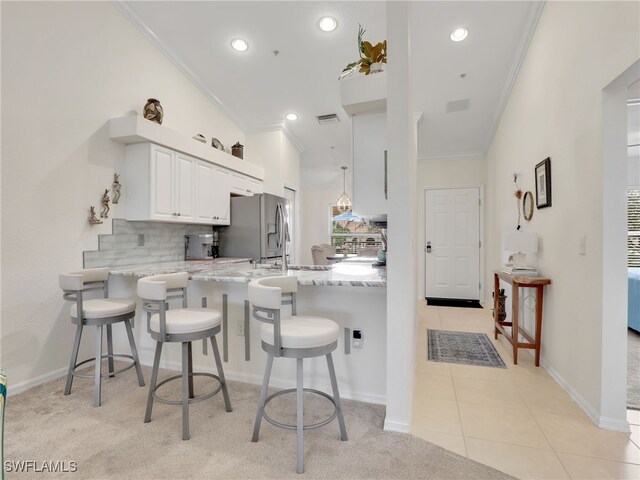 kitchen with white cabinets, light tile patterned floors, ornamental molding, kitchen peninsula, and a breakfast bar area